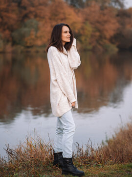 beautiful smiling young brunette woman in a long warm white sweater on the background of an autumn landscape