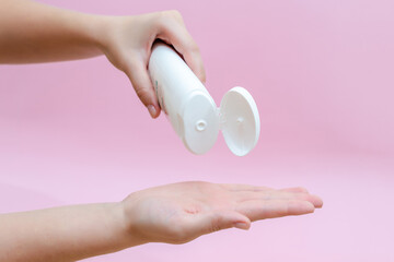 Womans hand pouring body lotion isolated on pink background. Beauty concept. Tube for cosmetic products