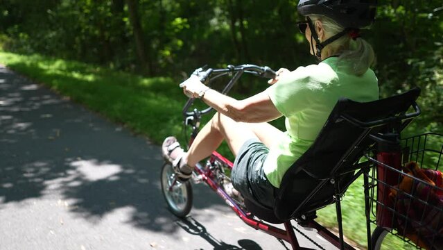 Slow motion of elderly woman riding recumbent bike on a path on a sunny day in the forest.