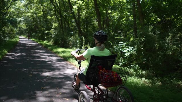 Slow motion of elderly woman riding recumbent bike on a path on a sunny day in the forest.