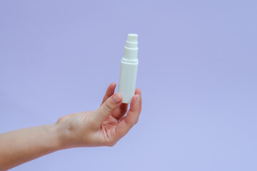 Womans hand holds a white tube (cream battle) for cosmetic products isolated on lilac background. Beauty concept