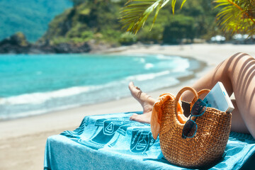 Woman legs lying on towel relaxing on summer holidays, near beach bag with a book and sunglasses on...