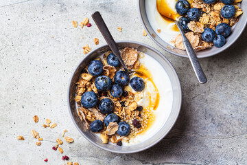 Breakfast yogurt bowl with granola, blueberries and maple syrup, gray background.