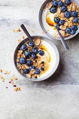 Breakfast yogurt bowl with granola, blueberries and maple syrup, gray background.