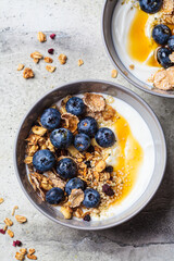 Breakfast coconut yogurt bowl with granola, blueberries and maple syrup, gray background.