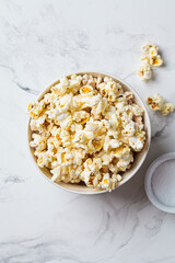 Salted popcorn in white bowl, white marble background.