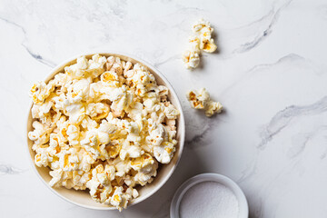 Salted popcorn in white bowl, white marble background.