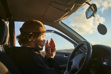 Naklejka premium Serious curly man lighting cigarette in his car, while preparing going to the beach