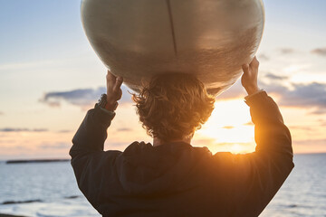 Man standing with long surfing board at his head while waiting on high waves at ocean beach