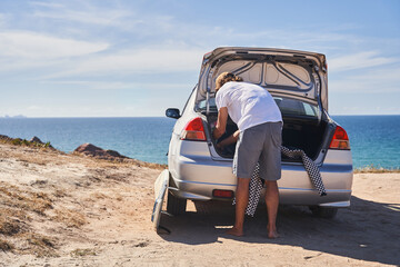 Young man taking surfing outfit from his car and preparing for the training
