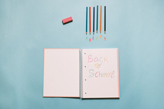 Back to school written in a notebook, with color pencils and eraser. Top view on a blue background