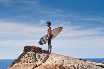 Surfer holding surfboard at the hands and looking at the sea surface