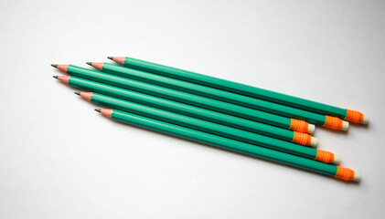 Pencils arranged in a pattern on white background. Graphite pencils green orange. School and office supplies isolated on white.
