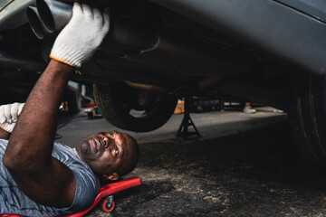 Male mechanic lying on creeper board and checking the car suspension.