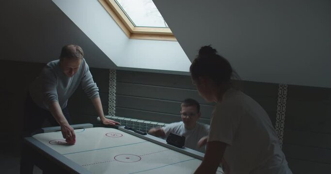 Young smiling male playing air hockey against young women, while their child standing near and cheering them up. High quality 4k footage