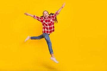 Fototapeta na wymiar Photo of excited pretty schoolgirl wear checkered shirt jumping high walking empty space isolated yellow color background