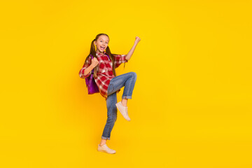 Photo of sweet funky schoolgirl wear checkered shirt walking rising fists isolated yellow color background