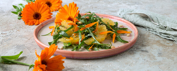 plate with vegetarian salad with arugula, orange and calendula flowers on a light table