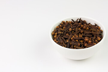 Cloves in white bowl isolated on white background, copy space. Herbal cloves have a fragrant and...