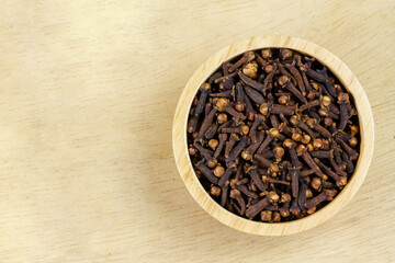 Cloves in wooden bowl on wooden background, top view, copy space. Herbal cloves have a fragrant and spicy flavor.