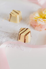 White chocolate candies and pale pink ribbon on white background. Gift, Love concept.