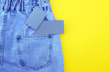Flat lay, detail of blue jeans with blank gray label on yellow background.