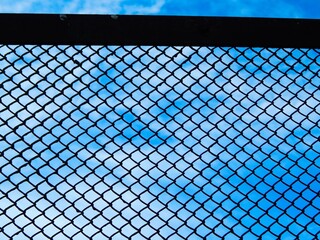 Fototapeta premium Metal grille on the background of a blue cloudy sky