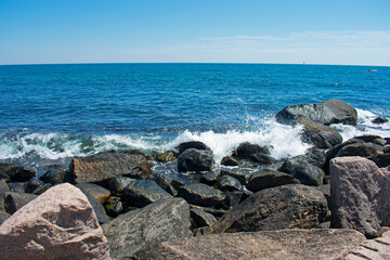 Fototapeta na wymiar Waves crashing into rocky shoreline in Westerly, Rhode Island, on a sunny day with blue skies -05