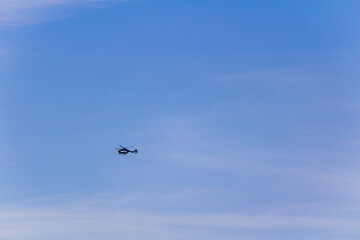 Black small helicopter flying against blue sky