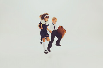 Portrait of cheerful pupils, boy and girl in school uniform running, jumping isolated over grey background