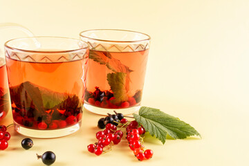 Tea made from berries and leaves of black and red currants in two transparent glasses (mugs, cups) on a yellow background. A useful alternative for colds and flu. Space for text.