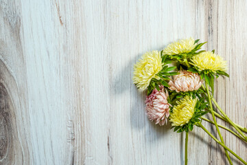 Bouquet of yellow and peach aster flowers placed at the bottom right of the image. Space for text. Light wood background.