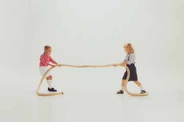 Portrait of two boys, children playing together, pulling the rope isolated over grey studio background