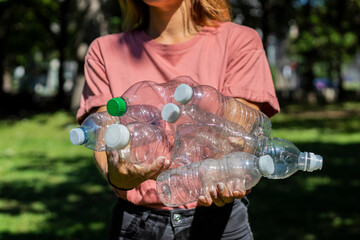 Pile of plastic bottle held by a young caucasian woman in a park during. sunny day, recycling and earth day
