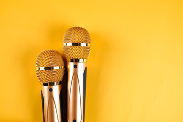 Two golden microphones isolated on yellow background close up - obrazy, fototapety, plakaty