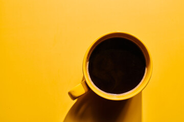 Cup of freshly brewed roasted coffee beans on yellow background
