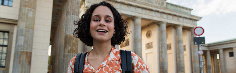 cheerful tourist with backpack standing near brandenburg gate in berlin, banner. © LIGHTFIELD STUDIOS
