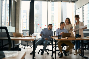 Colleagues are talking to each other in office with windows