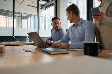 Colleagues men talking while sitting at table with laptop