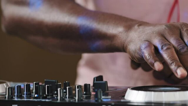 Unrecognizable african american male DJ man professional musician sound engineer with headphones and audio console panel mixer play live music at studio party create music set dancing set spin disc