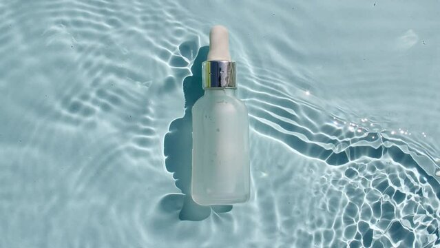 Cosmetic bottle, vial for oil, liquid, collagen serum on water surface with drops. Women's cosmetics skincare. Sample of layout of package beauty product. High quality 4k footage
