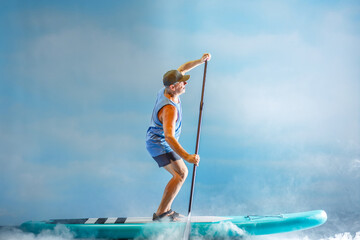 A man on a sub-board with an oar paddles in thick fog against the background of clouds.