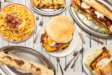 Set of dishes with wild food, big hamburger with egg, fried bacon and melted cheese, sandwich with the same ingredients, fries with cheese and bacon