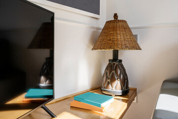 Corner of a living room with an oak wood tabletop with books, a natural lampshade lamp, a flat...