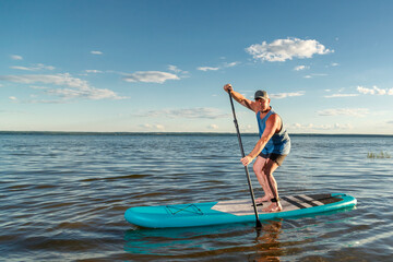 A man on a sup board against a clear blue sky.
