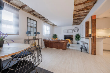 Living room of a studio apartment with open kitchen, exposed vintage wooden beams, brown leather...