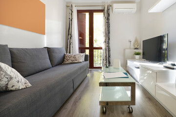 Living room of a holiday apartment with modern decoration with a coffee table on wheels, a white bookcase with a flat-screen TV and a three-seater fabric sofa