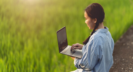 Asian woman farmer using laptop to store farm data In the evening with warm light. Agricultural technology concept. Organic agriculture.