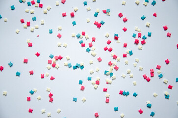 On a white sugar backing lies a sweet pastry topping in the form of pink hearts, orange, turquoise and red peas, and green, blue and yellow sticks