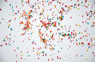 On a white sugar backing lies a sweet pastry topping in the form of pink hearts, orange, turquoise and red peas, and green, blue and yellow sticks